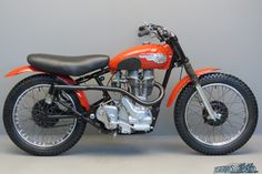 an orange and black motorcycle parked on top of a white floor next to a gray wall