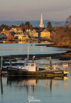 two boats are docked in the water next to some houses and buildings with a steeple in the background