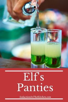 two glasses filled with liquid sitting on top of a table next to a person pouring green liquid