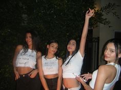 four women in white shirts are posing for the camera with their arms up and one woman is holding her hand up