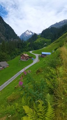 the road is winding and there are many houses in the valley behind it with mountains in the background