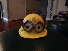 a yellow helmet with googly eyes sitting on top of a black ottoman