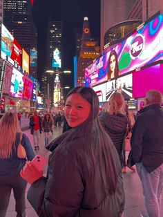 a woman standing in the middle of a busy city street at night with people walking around