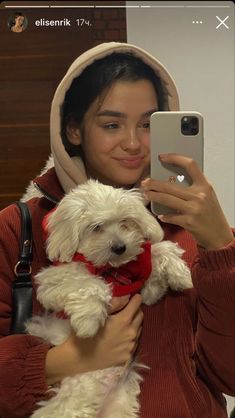 a woman taking a selfie with her phone while holding a white dog in her arms