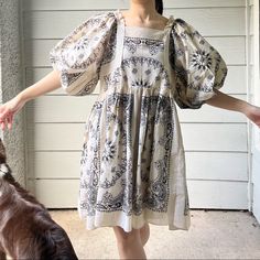 a woman in a dress standing next to a brown and white dog on a porch