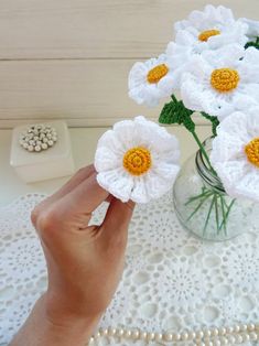 a person holding flowers in a vase on a doily with pearls around the edges