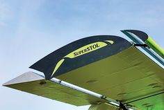 the underside of a green and black propellor airplane against a clear blue sky