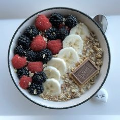 a bowl filled with oatmeal and fruit next to a spoon on a table