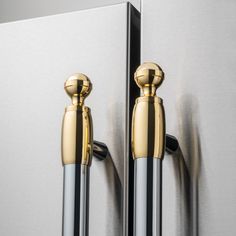 two golden handles are on the back of a silver refrigerator freezer with mirrored glass doors