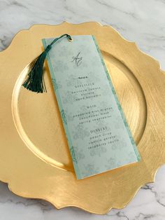 a gold plate with a green and white menu card on it, sitting on a marble table