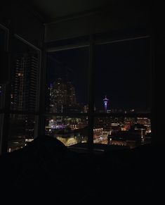 a view of the city at night from a window in a room with dark walls