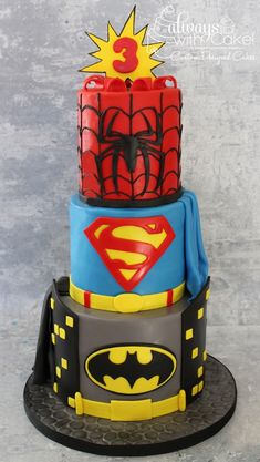 a three tiered cake with batman and spiderman decorations