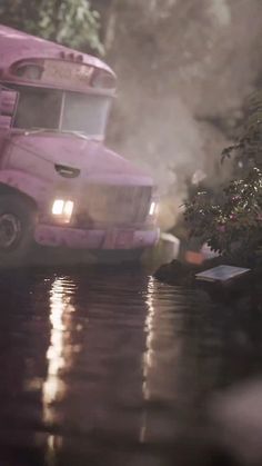 a pink truck is driving down the street in the rain with its lights turned on