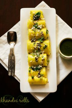 a white plate topped with ravioli next to a cup of green tea and a spoon