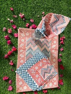 two pieces of cloth laying on the ground with pink flowers in the grass behind them