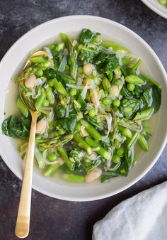 a white bowl filled with green vegetables on top of a table next to a wooden spoon