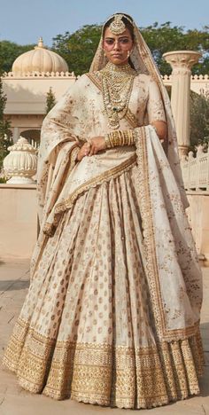 a woman in a white and gold bridal gown posing for the camera with her hands on her hips