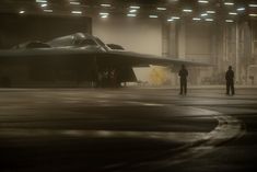 two men standing in front of a fighter jet