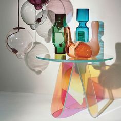 several vases and glass items on a table in front of a white wall with shadows