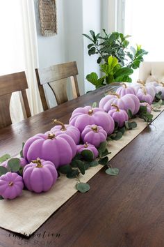 purple pumpkins lined up on a table in the middle of a long row with greenery