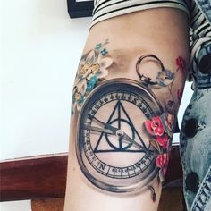 a woman's leg with a compass tattoo on it and flowers around the legs