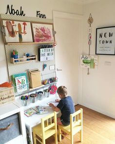 a young boy sitting at a table in front of a wall mounted art work area