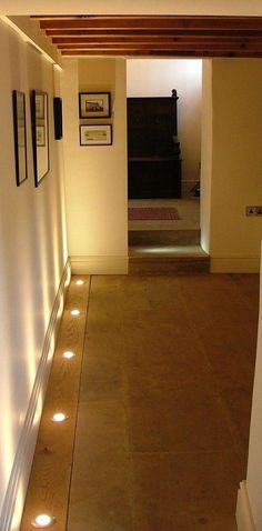 an empty hallway with lights on the floor and pictures hanging on the wall behind it