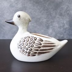 a white ceramic duck sitting on top of a wooden table next to a gray wall