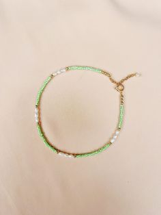 a bracelet with pearls and green beads on a white tablecloth, next to a gold - plated chain