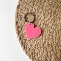 a pink heart shaped keychain sitting on top of a piece of jute