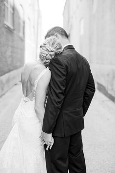 a bride and groom kissing in an alleyway on their wedding day, black and white photo