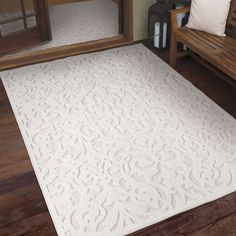 a large white rug sitting on top of a wooden floor next to a bench and mirror