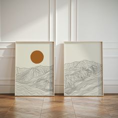 two framed art pieces on the floor in front of a white wall with a brown circle