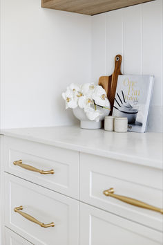 a white kitchen with gold handles and brass handles on the countertop, next to a cookbook