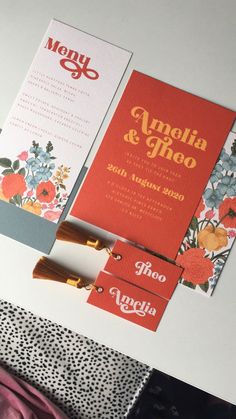 an orange and red wedding card with flowers on the front, and two matching envelopes