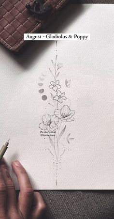 a person is writing on paper with a pen and some flowers in the corner next to it