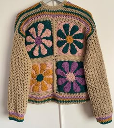 a crocheted jacket is hanging on a white coat hanger and it has flowers in the center