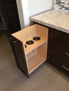 an open cabinet in the middle of a kitchen with two bowls and one cup holder