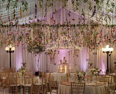 an indoor wedding venue decorated with flowers and greenery hanging from the ceiling, surrounded by tall chandeliers