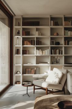 a living room filled with lots of white furniture and bookshelves next to a window