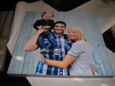 a man and woman holding a baby in front of a photo on a table top