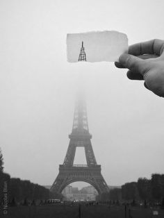 someone holding up a piece of paper in front of the eiffel tower