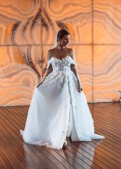 a woman in a white wedding dress standing on a wooden floor with an artistic wall behind her