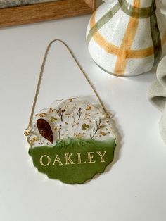 a ceramic ornament with the name oakley hanging from a string on a table