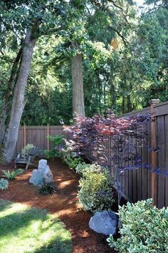 a fenced in yard with trees and plants on the side, next to a bench