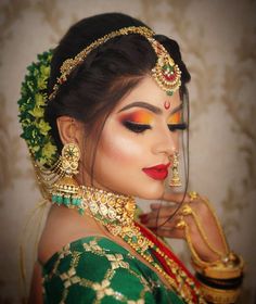 a woman in green and gold makeup looks down at her hand while wearing an elaborate head piece