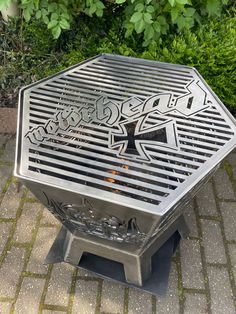 a metal fire pit sitting on top of a brick floor next to a green bush