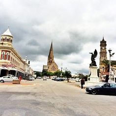 cars are parked on the street in front of some buildings and a clock tower with a steeple