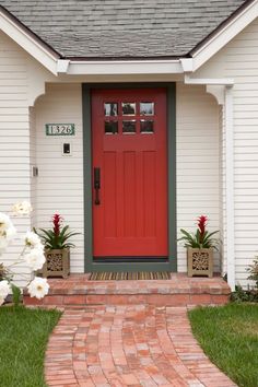 a red front door with brick walkway leading to it and white flowers in pots on either side