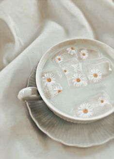 a white cup filled with water and daisies on top of a saucer